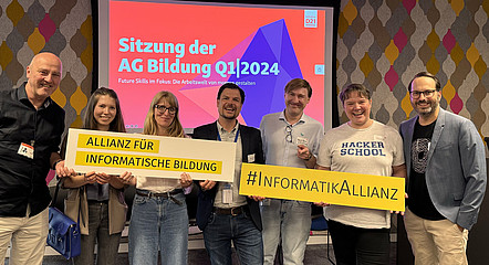 Sieben Personen stehen in einer Reihe und halten Schilder hoch, auf denen draufsteht "Allianz für informatische Bildung" "#InformatikAllianz"